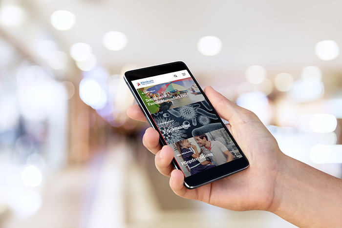 Man`s hand holding mobile smart phone with blank screen at blurred shopping mall background.