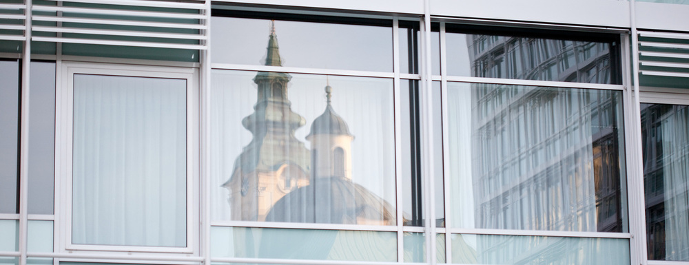 Das Bild zeigt die Fassade eines Ordensspitals in der sich eine Kirche spiegelt