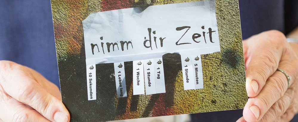 Das Bild zeigt Hände, die eine Karte halten mit der Aufschrift 'Nimm dir Zeit'